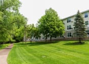 Thumbnail 34 of 34 - a grassy area with trees and a building in the background  at Briarcliff Apartments, a 55+ Community, Mahtomedi, MN, 55115