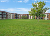 Thumbnail 56 of 56 - a grassy area with a tree in front of an apartment building