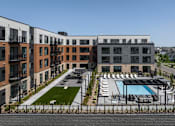 Thumbnail 1 of 61 - A modern apartment complex with a pool and a fenced-in parking area.