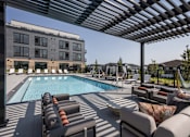 Thumbnail 52 of 61 - A pool area with sun loungers and a building in the background.