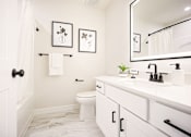 Thumbnail 11 of 15 - A white bathroom with a toilet, sink, and mirror.