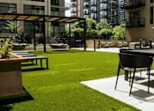 Thumbnail 45 of 77 - A patio with a table and chairs is surrounded by a grassy area and buildings.at Viridium Apartments, Minneapolis, MN 