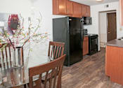 Thumbnail 10 of 28 - A black refrigerator sits in a kitchen with wooden cabinets and a glass table.