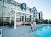 Thumbnail 23 of 80 - A pool area with a white pergola and a black fence at The Barnum Apartments, White Bear Lake