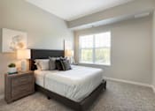 Thumbnail 37 of 80 - A bedroom with a large bed, nightstand, and window at The Barnum Apartments, White Bear Lake, Minnesota
