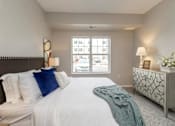 Thumbnail 49 of 80 - A bedroom with a large bed, a nightstand, and a window with a view of the street at The Barnum Apartments, White Bear Lake, Minnesota