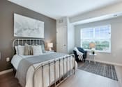 Thumbnail 59 of 80 - A bedroom with a large bed and a chair by the window at The Barnum Apartments, White Bear Lake, Minnesota