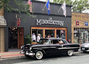 Thumbnail 74 of 80 - A black vintage car is parked in front of a building with a sign that says at The Barnum Apartments, White Bear Lake