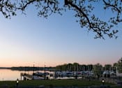 Thumbnail 77 of 80 - A tree branch is in the foreground of a serene lake scene with boats docked at a pier at The Barnum Apartments, MN, 55110