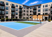 Thumbnail 62 of 110 - A tennis court is located in front of a large apartment building.