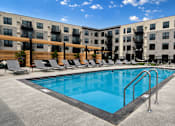 Thumbnail 66 of 110 - A swimming pool is surrounded by lounge chairs in front of apartment buildings.