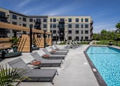Thumbnail 62 of 92 - A swimming pool surrounded by lounge chairs and a building in the background.