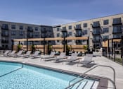 Thumbnail 61 of 92 - A swimming pool is surrounded by lounge chairs in front of apartment buildings.