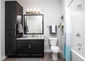 Thumbnail 58 of 81 - A bathroom with a white toilet, a sink with a mirror above it, and a shower with a blue shower curtain.
