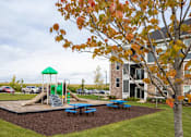 Thumbnail 65 of 81 - A playground with a green slide and a tree with orange leaves.