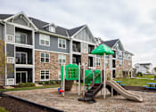 Thumbnail 66 of 81 - A playground with a green umbrella and slide in front of apartment buildings.
