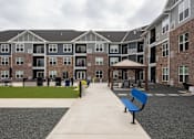 Thumbnail 67 of 81 - A long concrete walkway leads to a building with a blue bench on the right side.