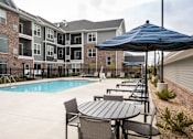 Thumbnail 75 of 81 - A pool area with a table and chairs and umbrella in front of apartment buildings.