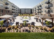 Thumbnail 1 of 32 - A courtyard with a grassy area, benches, and trees surrounded by apartment buildings at The Edison at Rice Creek I and II, Shoreview, MN 55126