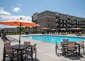 Thumbnail 2 of 24 - A pool area with chairs and umbrellas in front of a building at The Edison at Woodbury, Woodbury, 55129