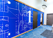 Thumbnail 19 of 20 - A hallway with a blue wall covered in architectural drawings.