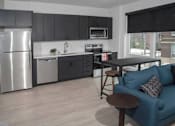 Thumbnail 34 of 47 - A modern kitchen with a blue couch and a wooden table at The Redwell Apartments, Minneapolis, MN