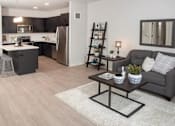 Thumbnail 37 of 47 - A modern kitchen with a grey couch and a coffee table in the foreground at The Redwell Apartments, Minneapolis, MN 55401