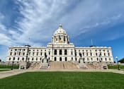 Thumbnail 36 of 54 - A large, stately building with a dome on top sits under a blue sky with scattered clouds.