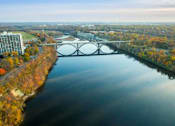 Thumbnail 38 of 54 - A bridge spans a river in a city with trees in the background.