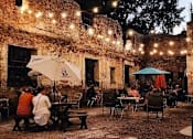Thumbnail 45 of 54 - A group of people are sitting at tables under umbrellas in an outdoor seating area.