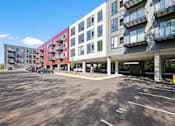 Thumbnail 46 of 54 - A parking lot in front of a multi-story building with cars parked.
