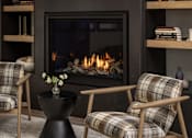 Thumbnail 11 of 55 - A fireplace with a fire burning inside and two chairs with plaid upholstery in front of it.