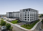 Thumbnail 60 of 70 - A modern multi-story building with a parking lot in front.