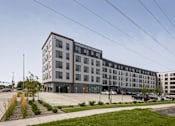Thumbnail 61 of 70 - A modern multi-story building with a parking lot in front.