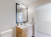 Thumbnail 11 of 49 - A bathroom with a toilet, sink, mirror, and lights.