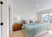 Thumbnail 9 of 49 - A bedroom with a bed, nightstand, and lamp.