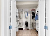 Thumbnail 55 of 123 - A white walk in closet with clothes hanging on shelves.