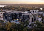 Thumbnail 55 of 64 - A large apartment complex is surrounded by trees and is lit up at dusk.