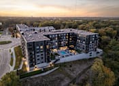 Thumbnail 56 of 64 - A modern apartment complex with a pool and surrounded by trees.