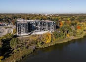 Thumbnail 43 of 64 - A large building sits next to a body of water with trees in the background.