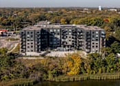 Thumbnail 44 of 64 - A large grey building with a lot of windows is surrounded by trees with yellow leaves.