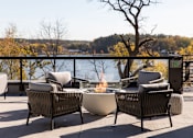 Thumbnail 48 of 64 - A patio with a fire pit and chairs overlooking a body of water.