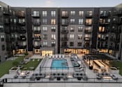 Thumbnail 52 of 64 - A modern apartment complex with a pool and outdoor seating area.