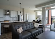 Thumbnail 13 of 45 - A black leather couch with a white pillow is in the middle of a kitchen and living room.