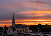 Thumbnail 31 of 45 - A church with a steeple is silhouetted against a sunset sky.