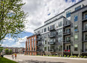 Thumbnail 64 of 69 - A modern apartment building with balconies and a person walking in front.
