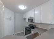 Thumbnail 8 of 23 - an empty kitchen with white cabinets and a stove and microwave at Warner Center Townhomes, California, 91303