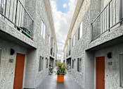 Thumbnail 15 of 19 - a courtyard between two buildings with orange doors and a potted plant at The Marq Apartments LLC, Los Angeles, California
