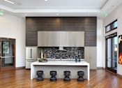 Thumbnail 12 of 60 - A modern kitchen with a white countertop and black stools. at Cirrus Redwood City Apartments, Redwood City