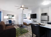 Thumbnail 2 of 21 - A modern living room with a brown sofa, a glass coffee table, a television, and a bed in the background. at The Maddox Sunnyvale Apartments, California, 94087